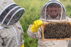 "Buzzing with Pride"A moment of pride as this beekeeper holds up the frame, sharing the thrill of beekeeping with a friend by their side.